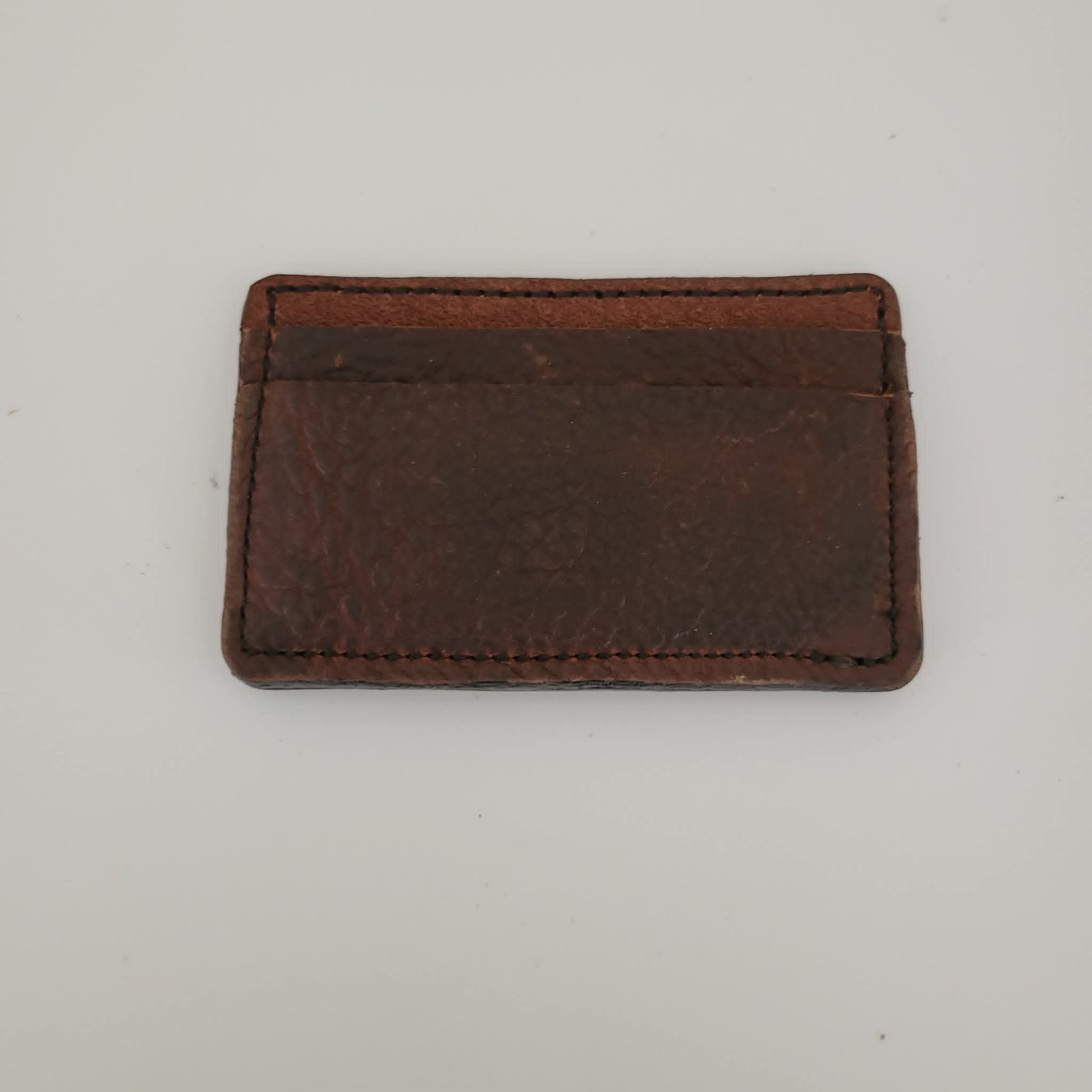 A small brown leather card holder or wallet with rounded corners and visible stitching, photographed on a plain light background.